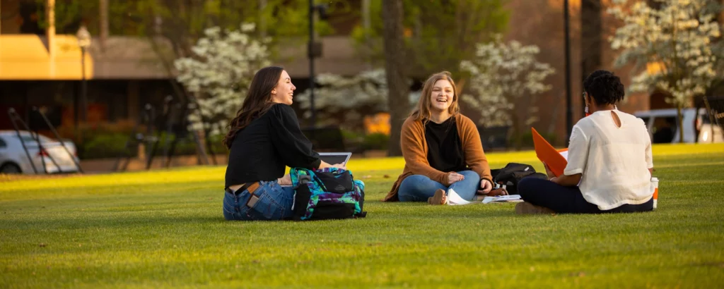 Three female students sitting on grass and talking