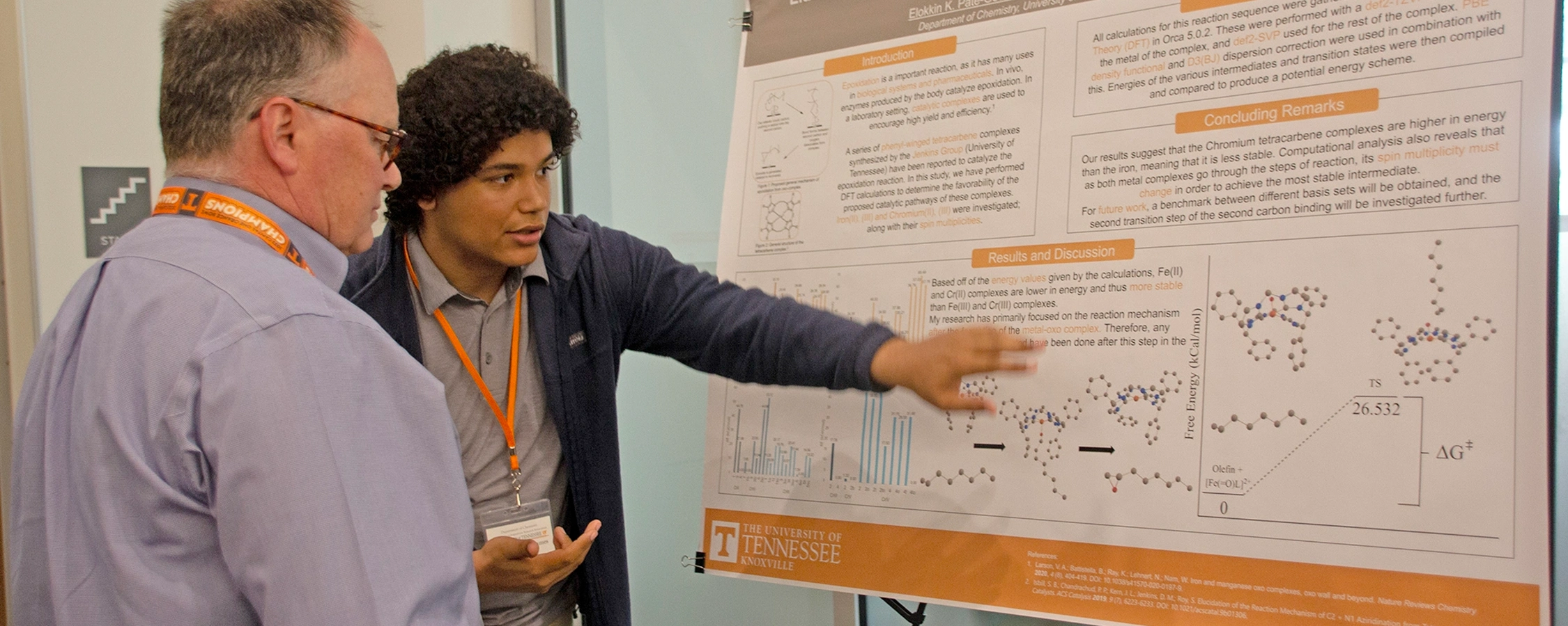 A student speaking with a professor points at a research poster