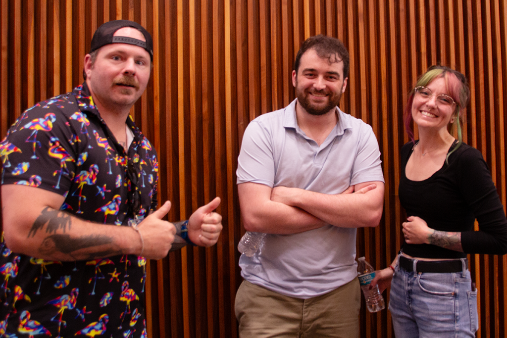 Three graduate students stand in front of a wall smiling at the camera.