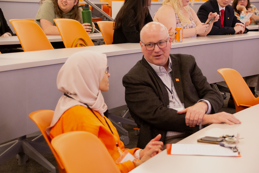 Dr. Kevin Shaughnessy is talking with Dr. Nahla Hatab at a table in the Mossman lecture hall after the oral presentation session of the symposium.