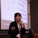 Vu (Lynn) Nguyen, winner of the oral presentation award, holds a lavalier microphone in one hand and a clicker in the other as she delivers her oral presentation.