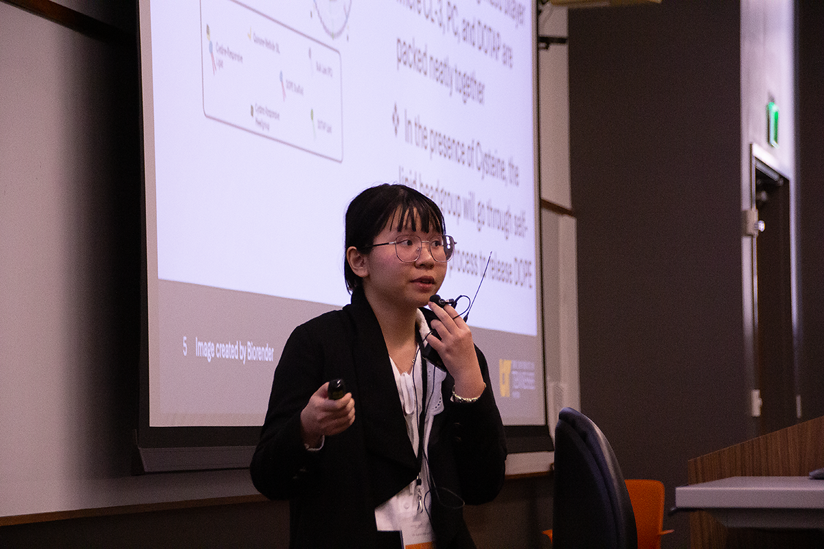 Vu (Lynn) Nguyen, winner of the oral presentation award, holds a lavalier microphone in one hand and a clicker in the other as she delivers her oral presentation.