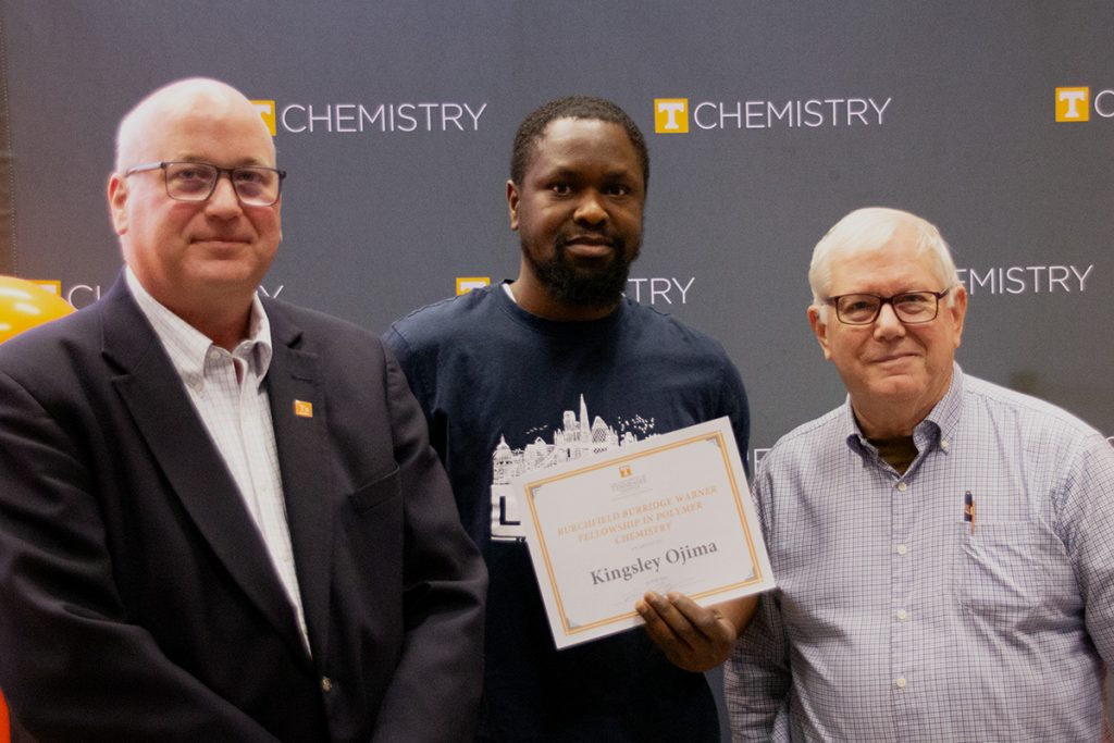 Kingsley Ojima stands with Dr. Shaughnessy and Tom Warner, holding the certificate for his award.